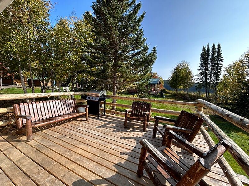 La terrasse en bois du chalet offre un espace de détente extérieur avec un barbecue et des bancs.