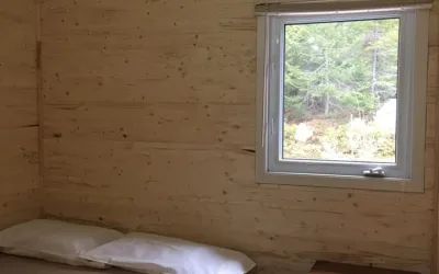 Vue sur la forêt depuis l'intérieur d'une chambre aux murs de bois du chalet Éliane.