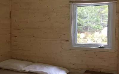 Vue sur la forêt depuis l'intérieur d'une chambre aux murs de bois du chalet Éliane.