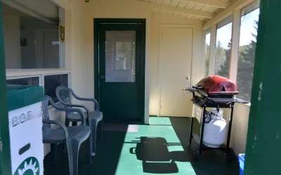 The enclosed porch of the Samuel cabin features a barbecue and chairs for your relaxing moments.