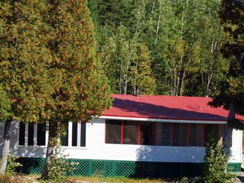 The Thérèse cottage features white siding, a red roof, and a screened-in porch.