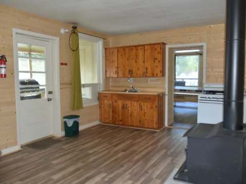 View of the kitchen and living area of Chalet Thérèse with wood stove and wooden cabinets.