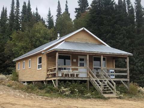 Le chalet numéro 12 est entouré de forêt avec une galerie couverte et des chaises extérieures.