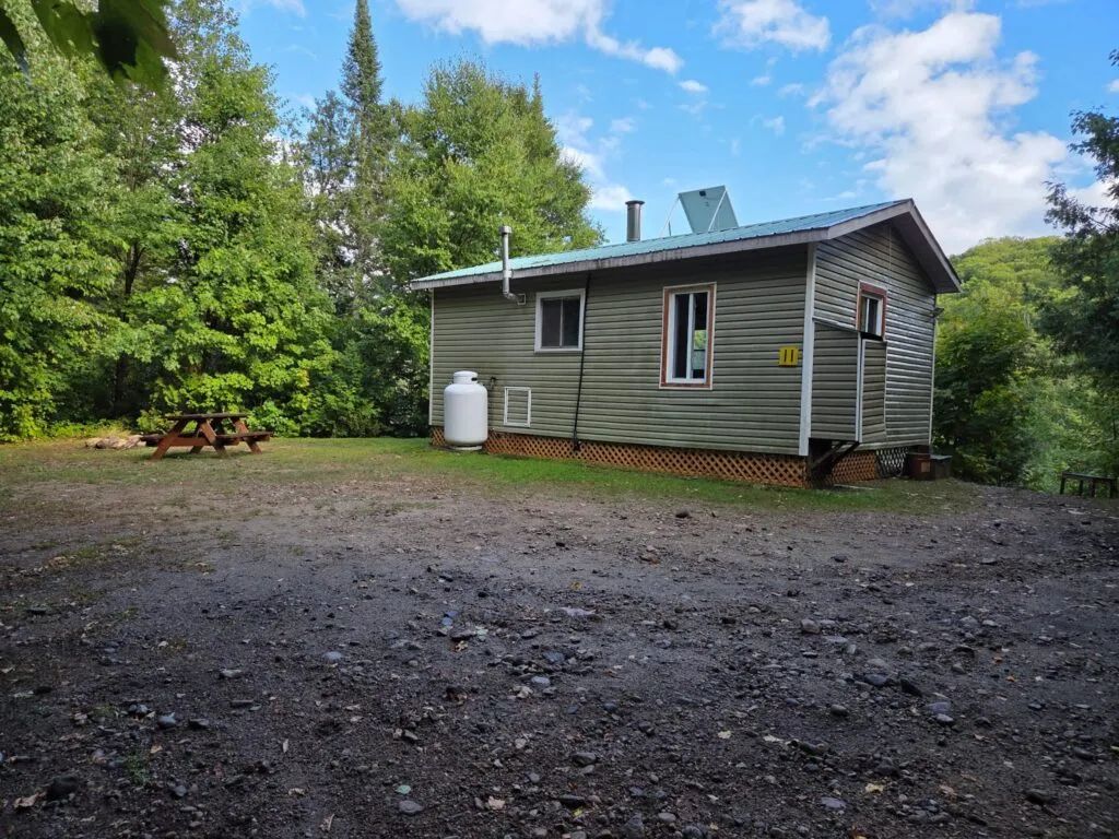 Vue extérieure du chalet 11 avec sa table de pique-nique adjacente dans un environnement boisé.
