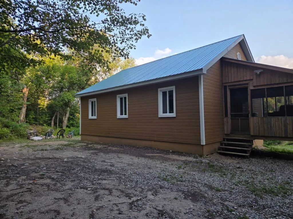 Vue latérale du chalet 12 avec son revêtement brun et sa véranda grillagée.
