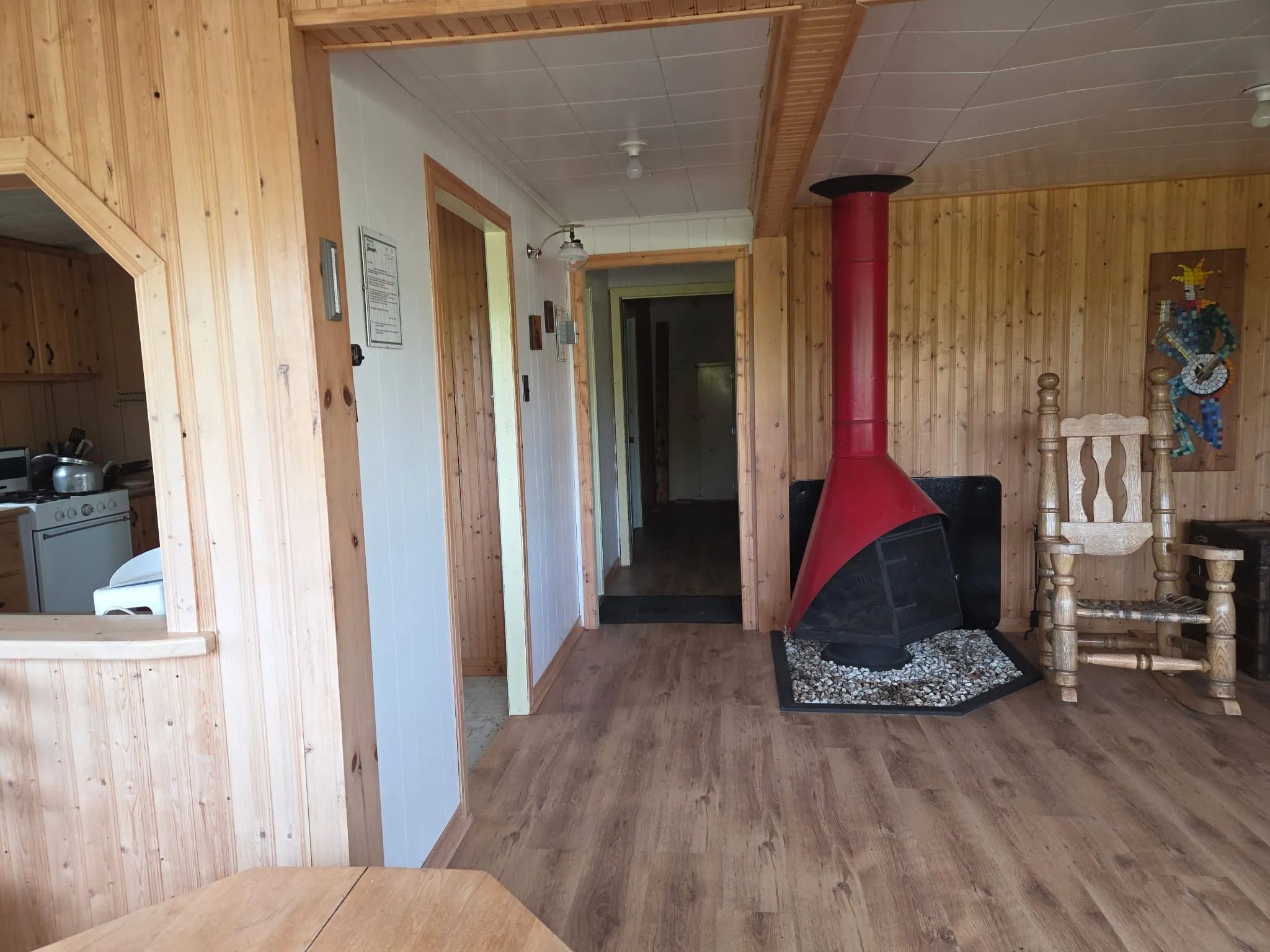 L'intérieur du chalet comprend un foyer rouge, une chaise berçante et un accès vers la cuisine.