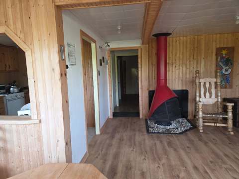 L'intérieur du chalet comprend un foyer rouge, une chaise berçante et un accès vers la cuisine.