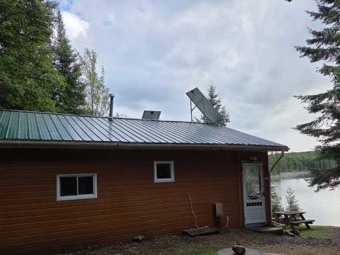 Vue latérale du chalet avec son toit métallique et ses panneaux solaires en bordure de lac.