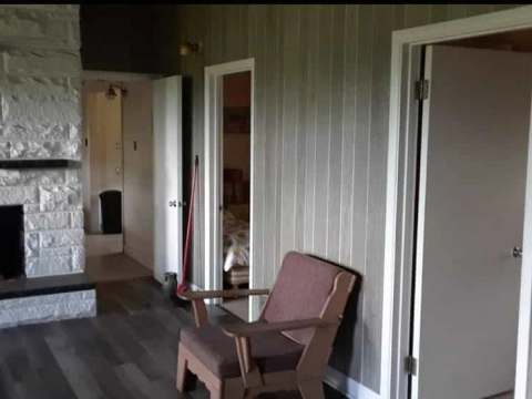 Vue du salon du chalet avec foyer en pierre et accès aux chambres.