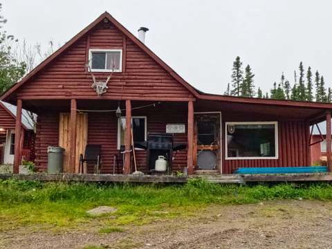 Vue extérieure du chalet en bois rond avec sa galerie et son barbecue.