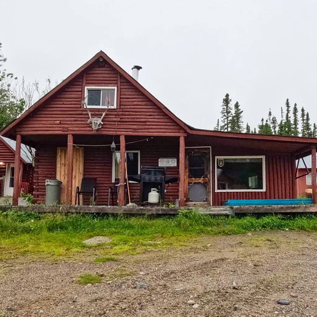 Vue extérieure du chalet en bois rond avec sa galerie et son barbecue.