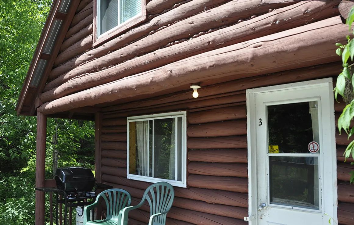 View of the cabin's front exterior with outdoor chairs and a barbecue.