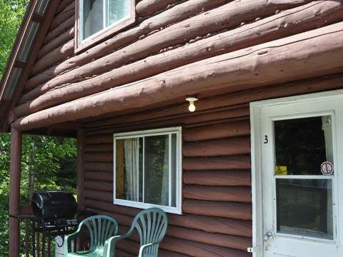 View of the cabin's front exterior with outdoor chairs and a barbecue.
