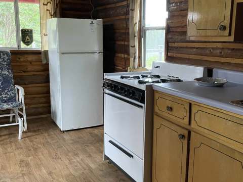 The rustic kitchen of chalet 1 includes a stove and a refrigerator in a log cabin setting.