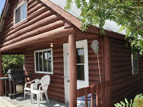 Exterior facade of cabin 2 with its porch, including chairs and a barbecue.