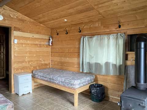 L'intérieur du chalet comprend un lit simple et un poêle à bois pour votre confort.