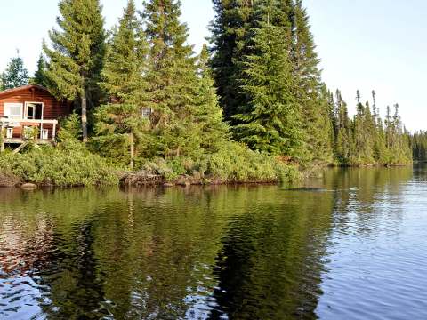 Vue sur le chalet en bordure de lac entouré de conifères.