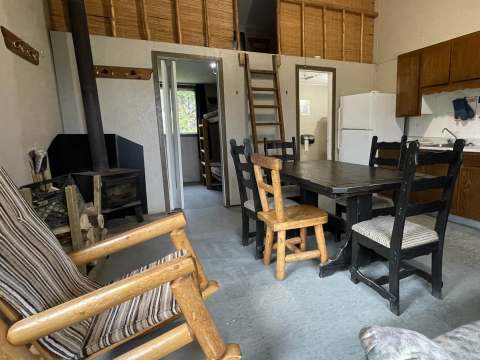 L'aire ouverte du chalet comprend une table à manger, un poêle à bois et un accès aux chambres.