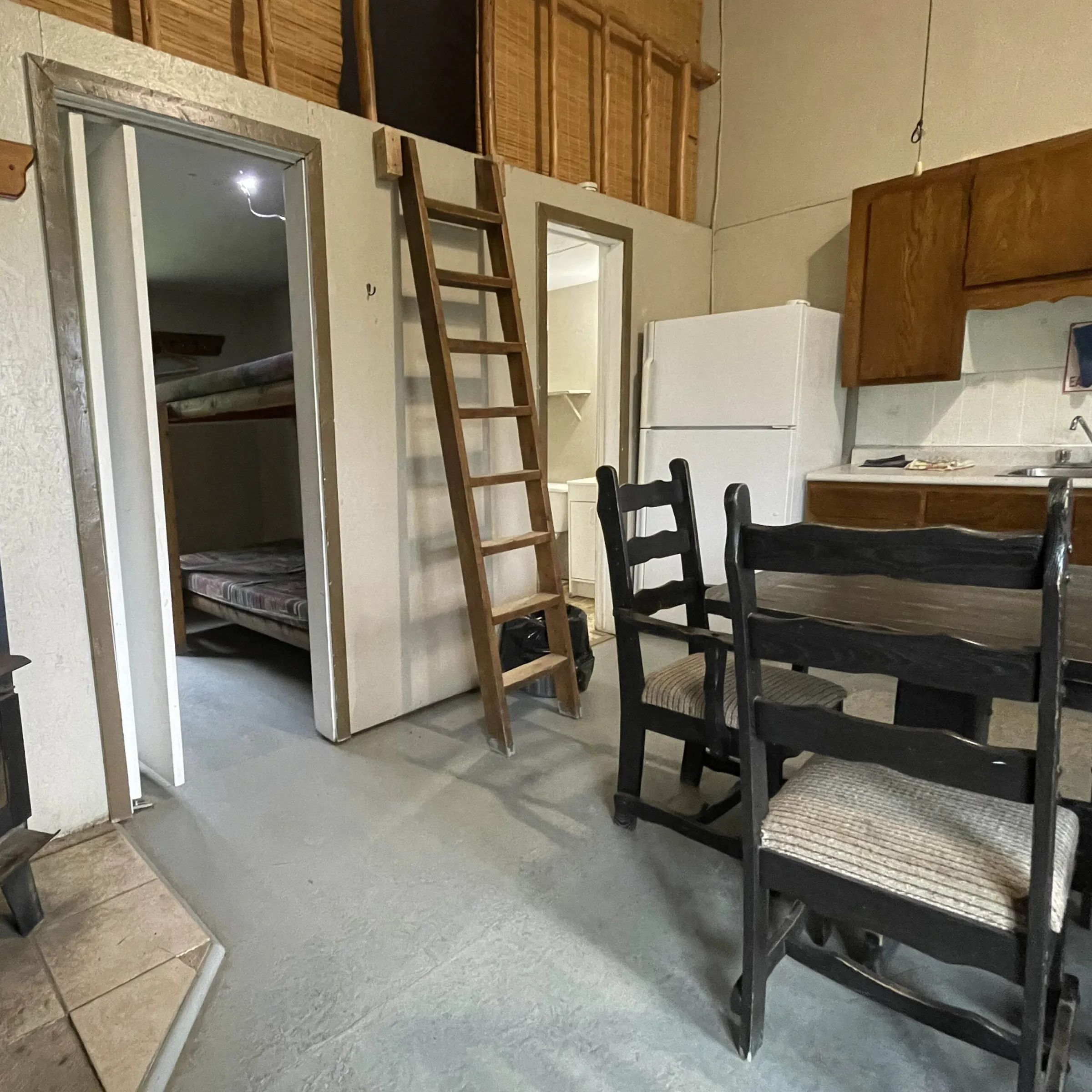 Vue intérieure du chalet comprenant une cuisine, un espace repas et une échelle menant à une mezzanine.