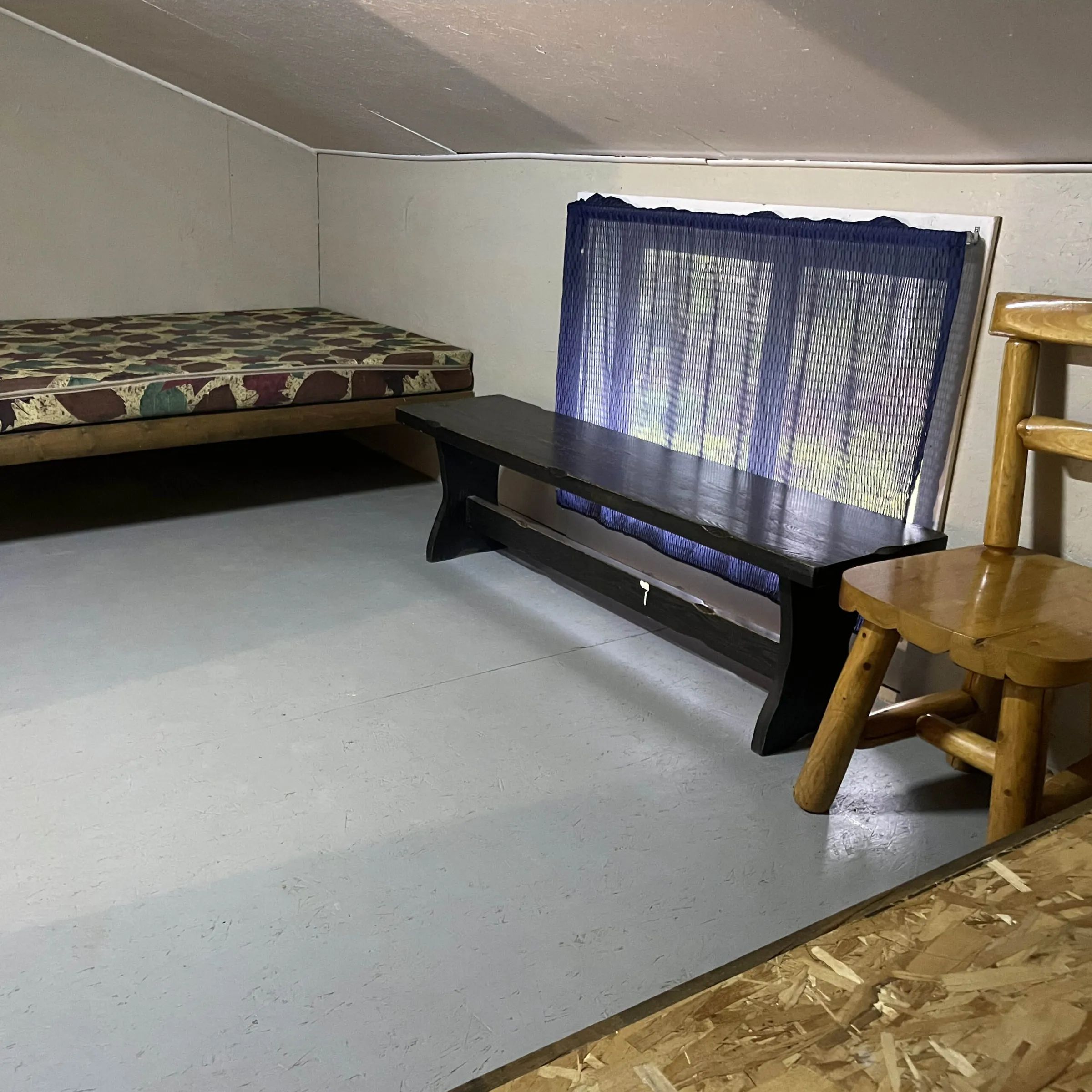 Vue de l'aménagement intérieur du chalet comprenant un lit, un banc et une chaise en bois.