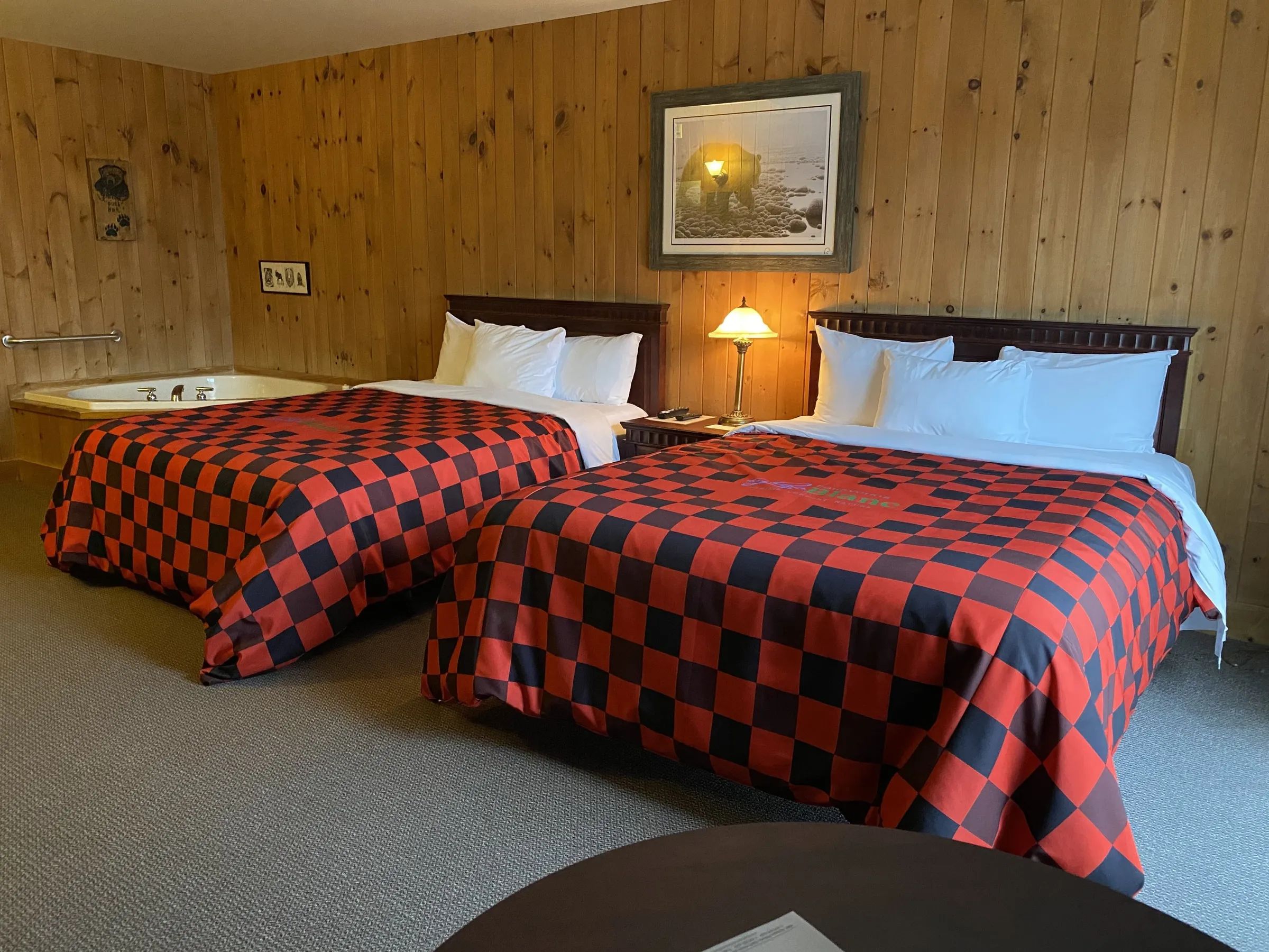 Cette chambre dispose de deux lits aux couvertures à carreaux rouges et noirs et d'un bain tourbillon.