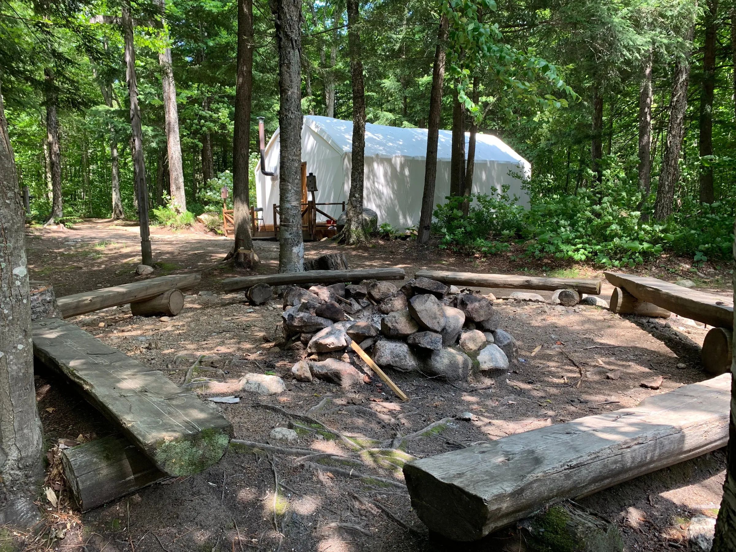 Un espace de feu de camp entouré de bancs devant une tente de style prêt-à-camper en forêt.