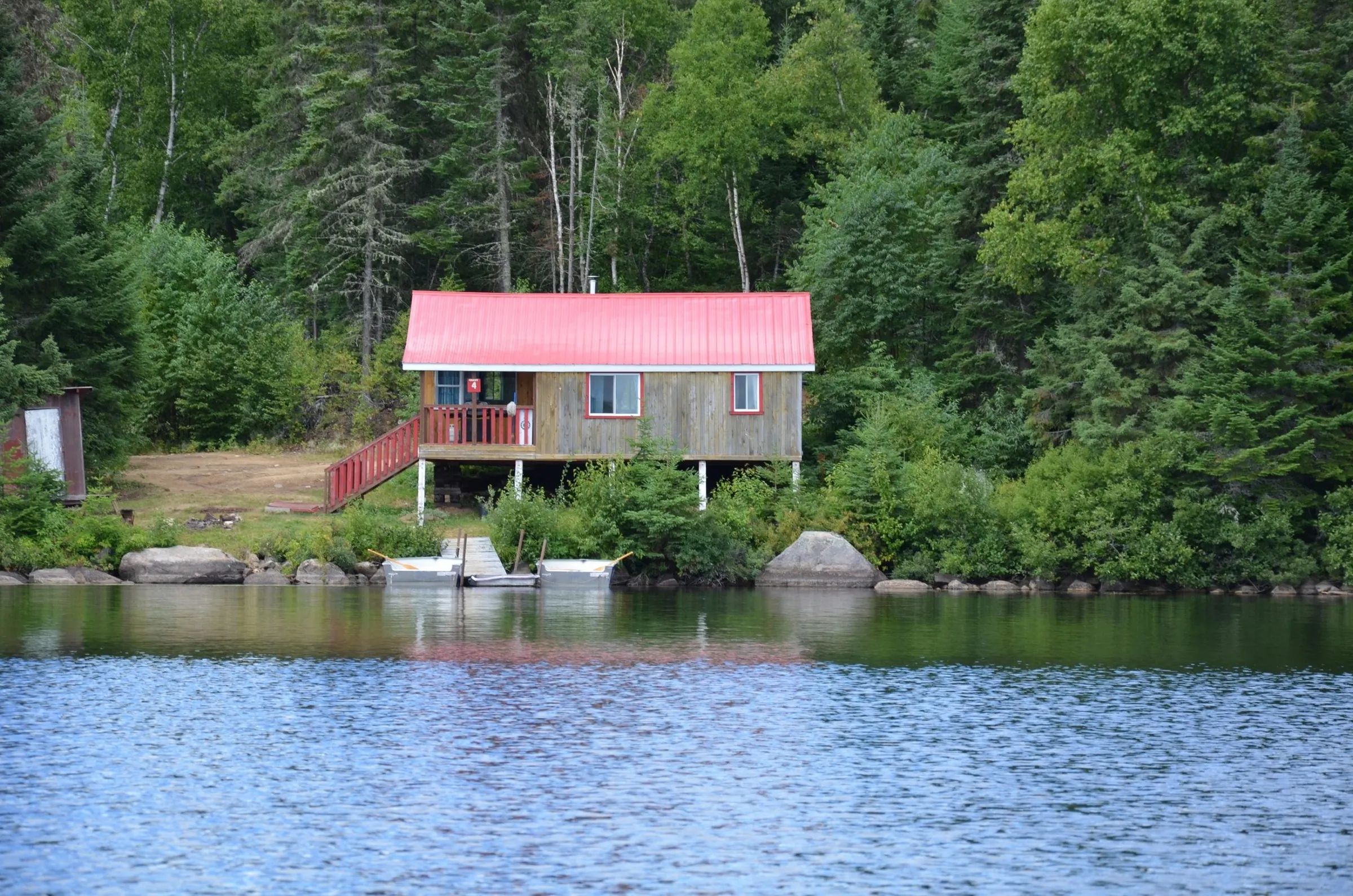 View of the cabin with its red roof located by the lake with a private dock.