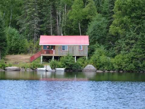 View of the cabin with its red roof located by the lake with a private dock.
