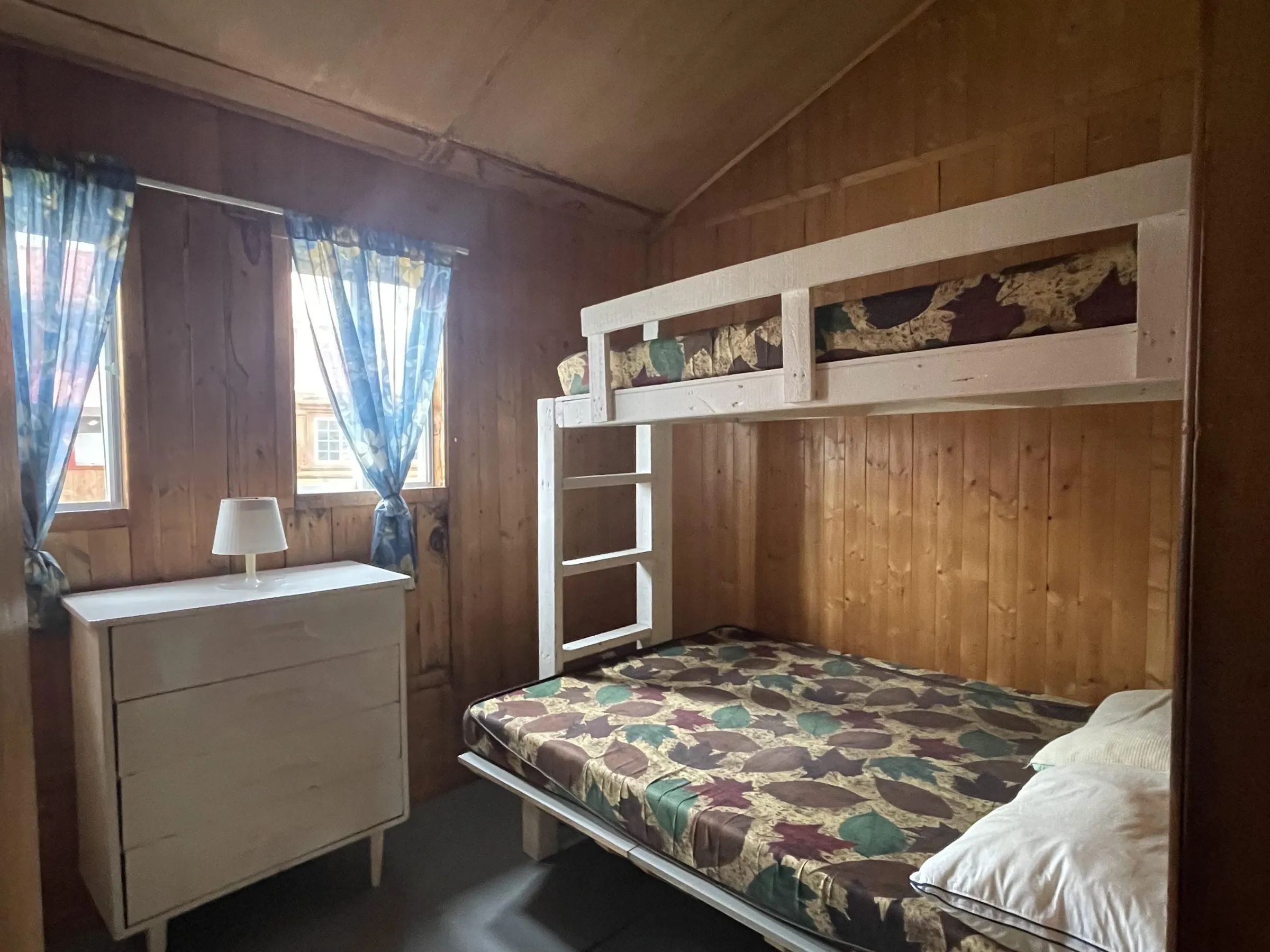 Cette chambre de chalet comprend un lit superposé et une commode en bois.