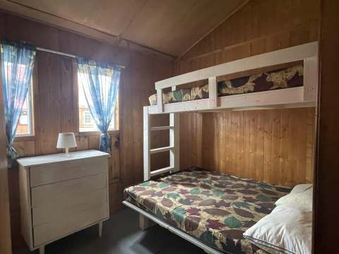 Cette chambre de chalet comprend un lit superposé et une commode en bois.