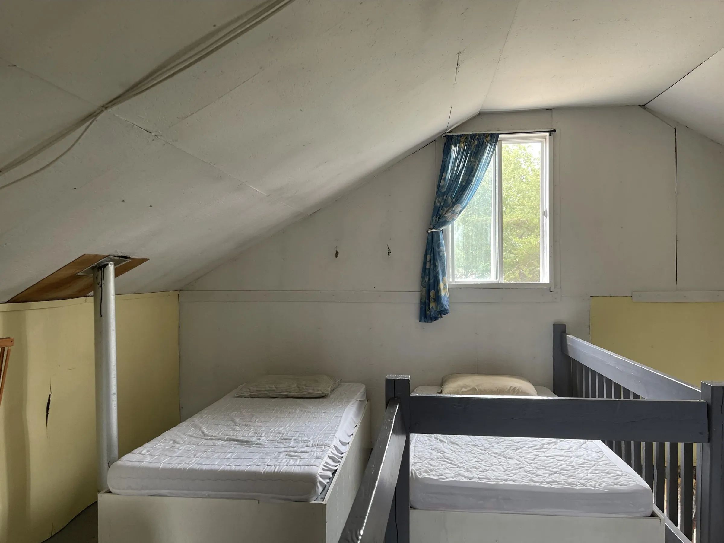 Deux lits simples sont disposés sous le plafond incliné de la mezzanine du chalet.