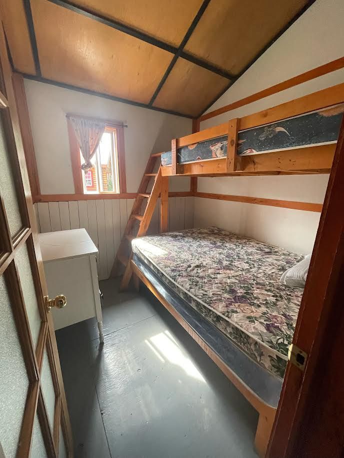 Cette chambre de chalet comprend un lit superposé avec une structure en bois et un petit meuble.