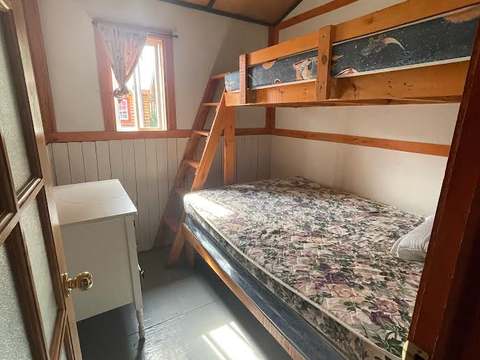 Cette chambre de chalet comprend un lit superposé avec une structure en bois et un petit meuble.