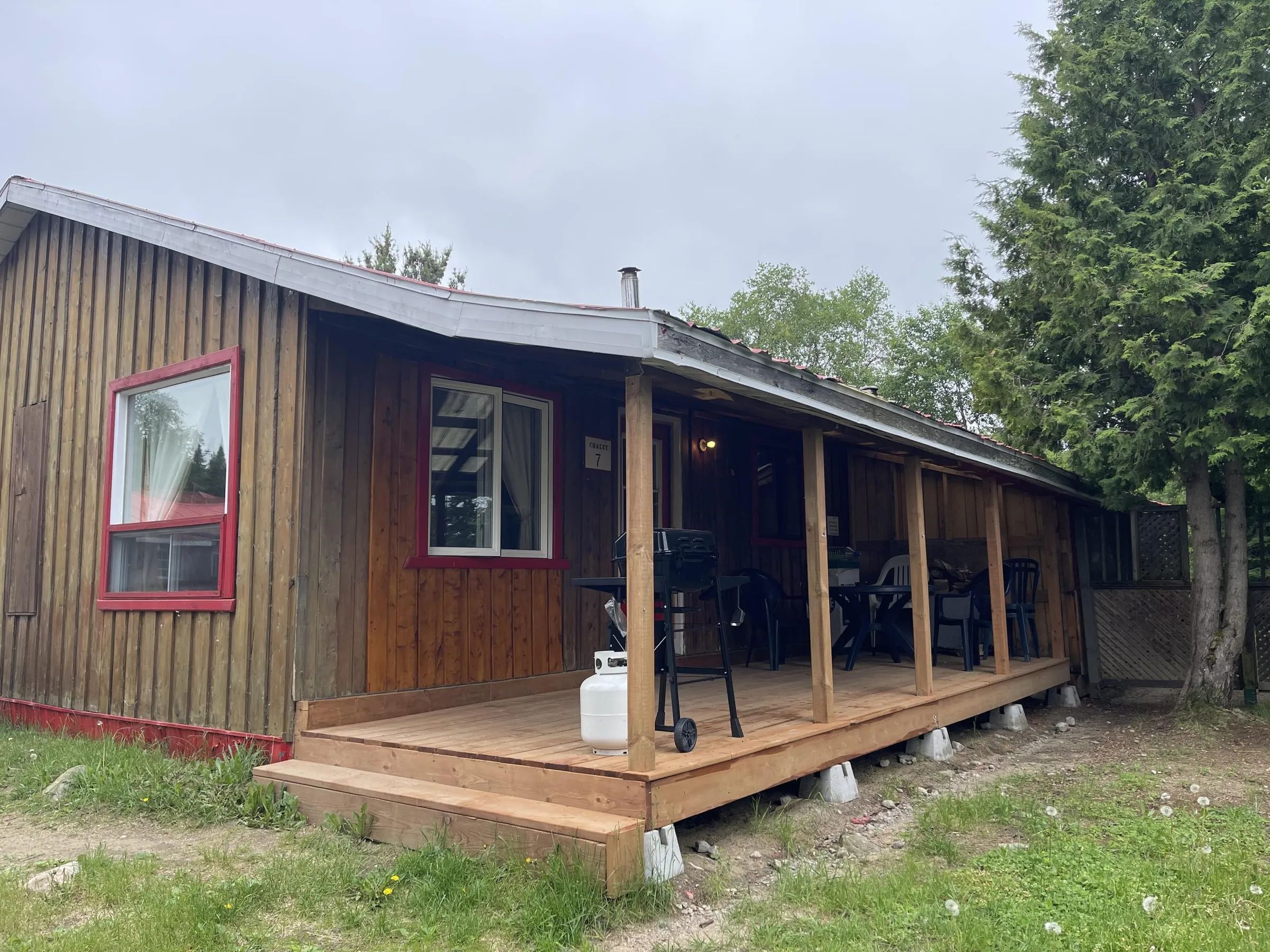 Vue latérale du chalet avec une galerie couverte équipée d'un barbecue et de mobilier d'extérieur.