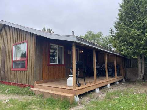 Vue latérale du chalet avec une galerie couverte équipée d'un barbecue et de mobilier d'extérieur.