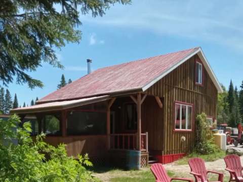 Vue extérieure du chalet 7 avec sa véranda et ses chaises Adirondack installées à proximité.