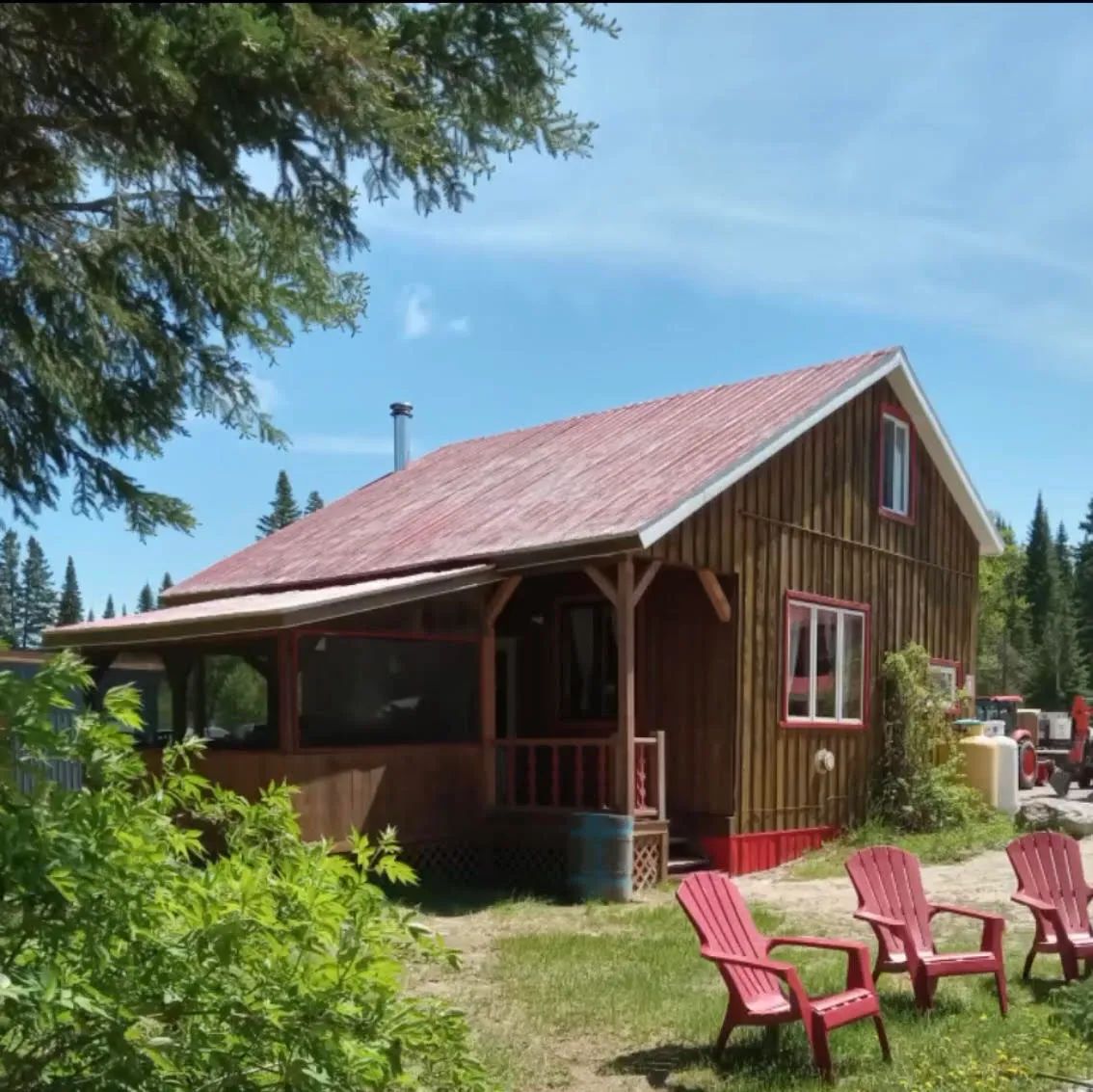 Vue extérieure du chalet 7 avec sa véranda et ses chaises Adirondack installées à proximité.