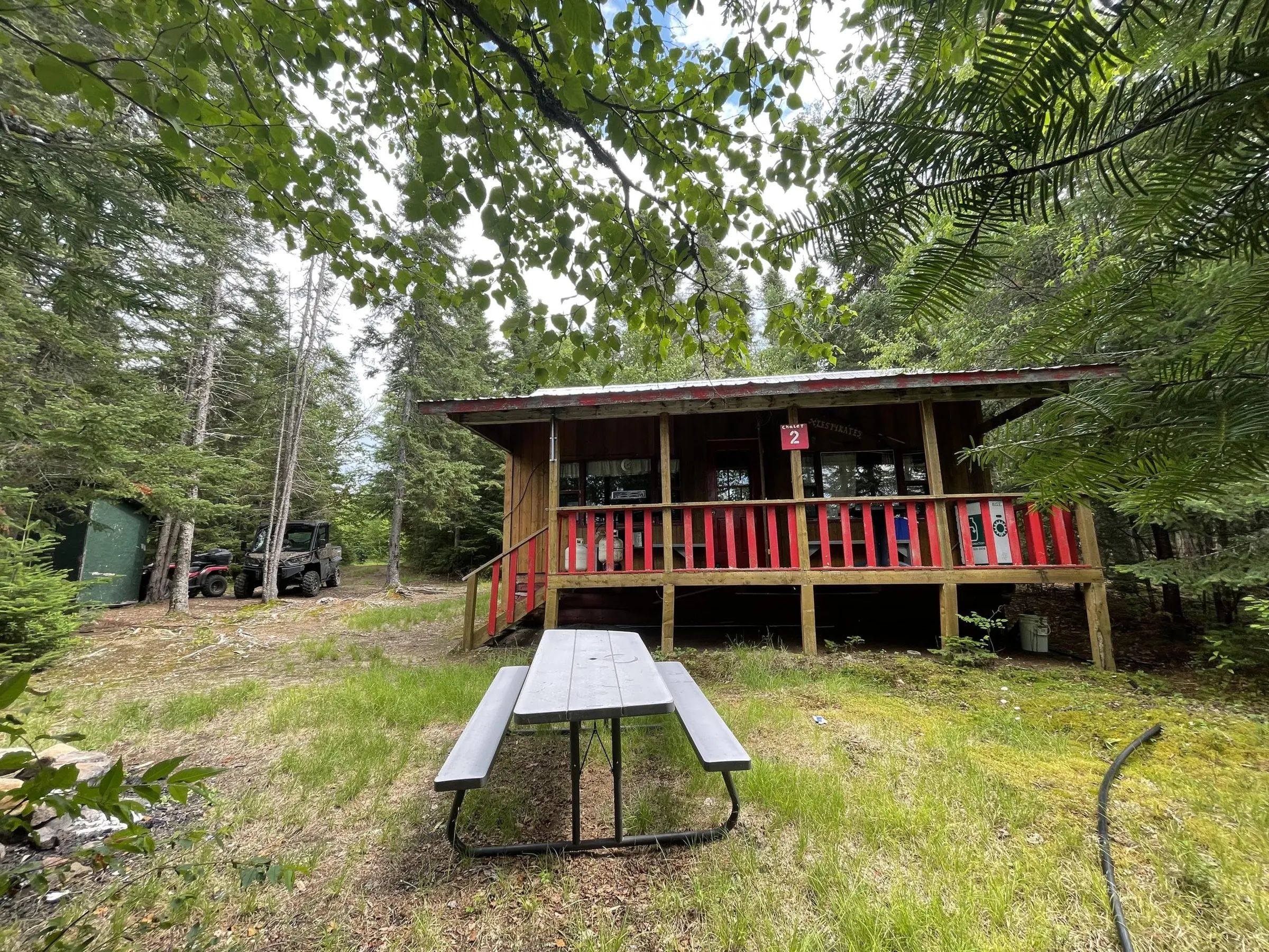 Chalet number 2 features a covered porch and a picnic table in the forest.