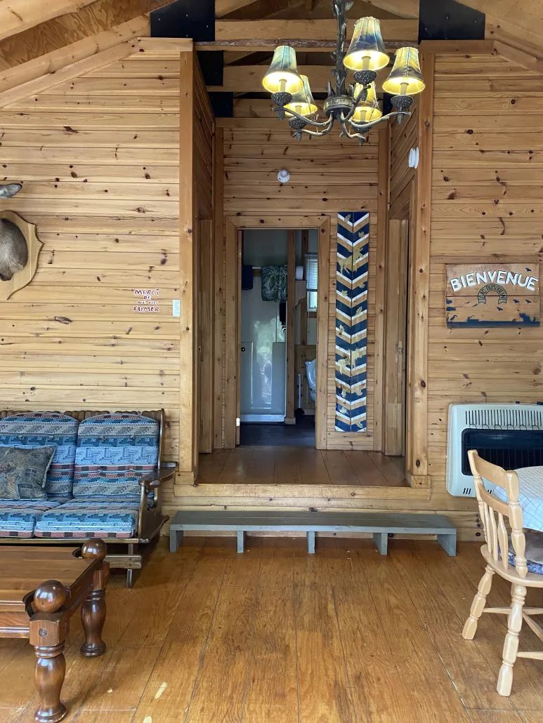 Vue de l'intérieur en bois rond du chalet avec son coin salon et son accès à la salle de bain.
