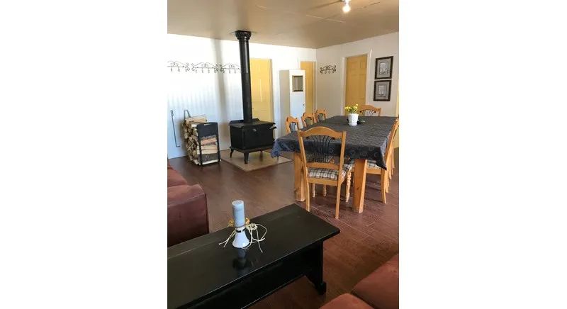 The cottage's living area includes a dining table and a wood stove.