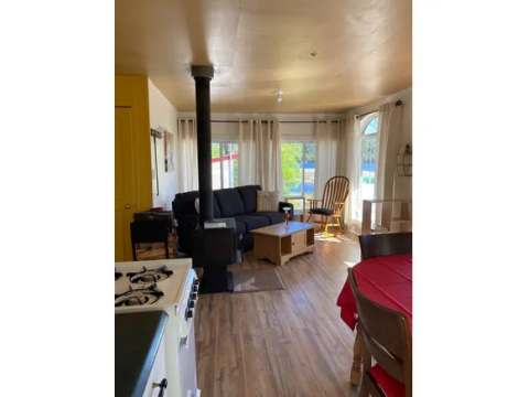 The cottage's living and dining area includes a wood stove, a sofa, and a dining table.