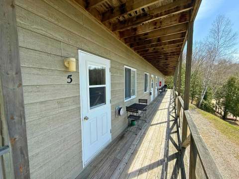 A small table and two chairs are set up on the deck in front of unit number five.