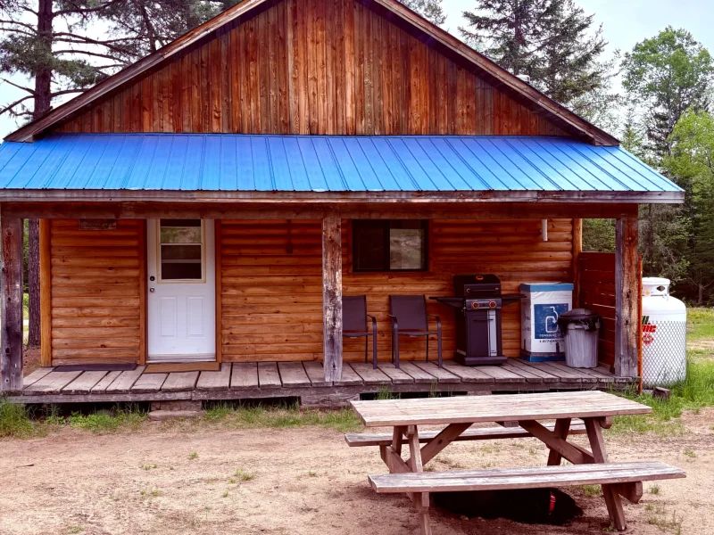 Vue extérieure du chalet de l'école avec sa galerie couverte, son barbecue et sa table de pique-nique.