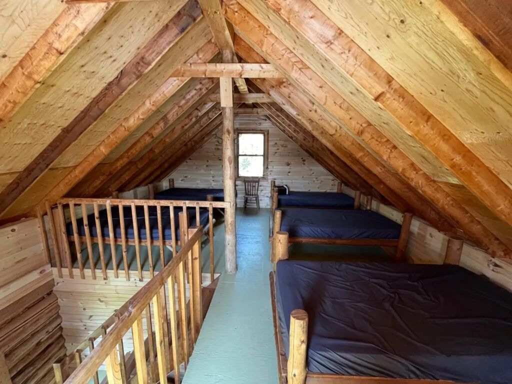 The loft of the Jolie chalet features several beds arranged under the wooden framework.