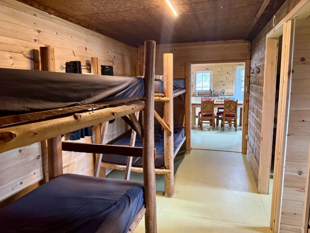 The bedroom features wooden bunk beds with a view into the cabin's dining area.