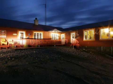 The lodge is illuminated in the evening, offering a welcoming atmosphere with its wooden deck.