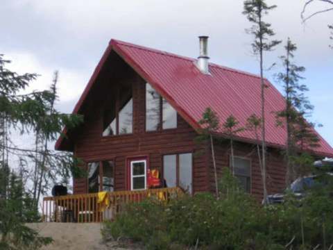 Vue extérieure du chalet en bois avec toit rouge et galerie au milieu de la forêt.