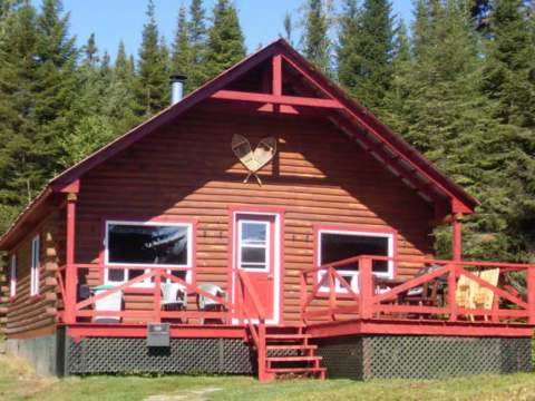 Façade extérieure du chalet en bois avec sa galerie et ses chaises de détente.