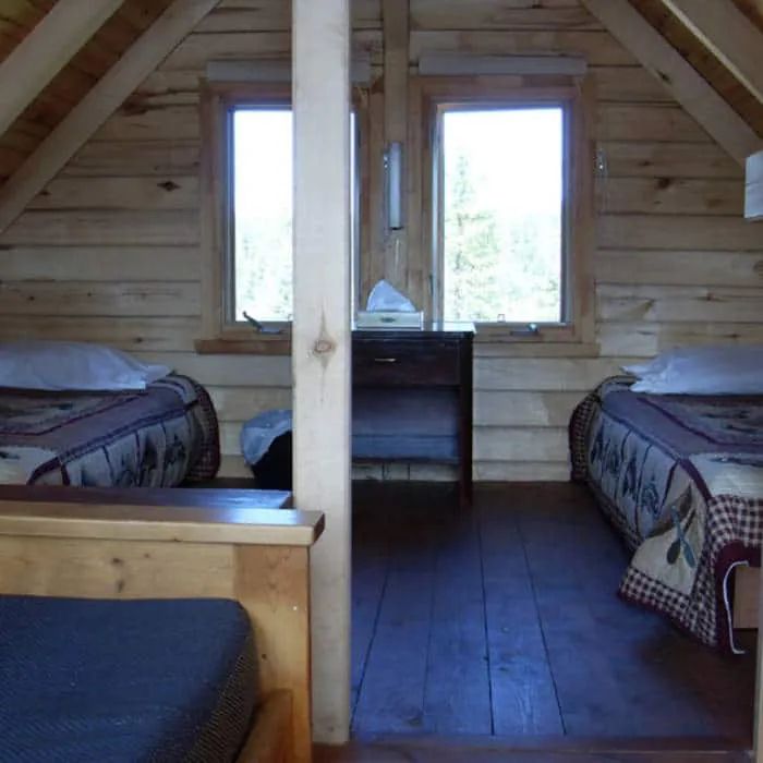 This bedroom under the cabin roof features two beds with a view of the surrounding forest.