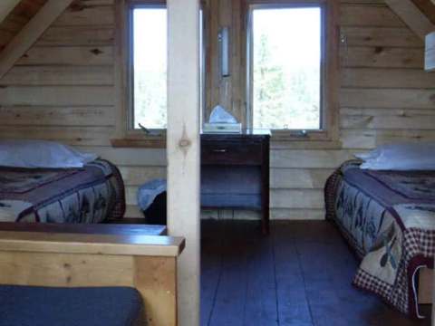 This bedroom under the cabin roof features two beds with a view of the surrounding forest.